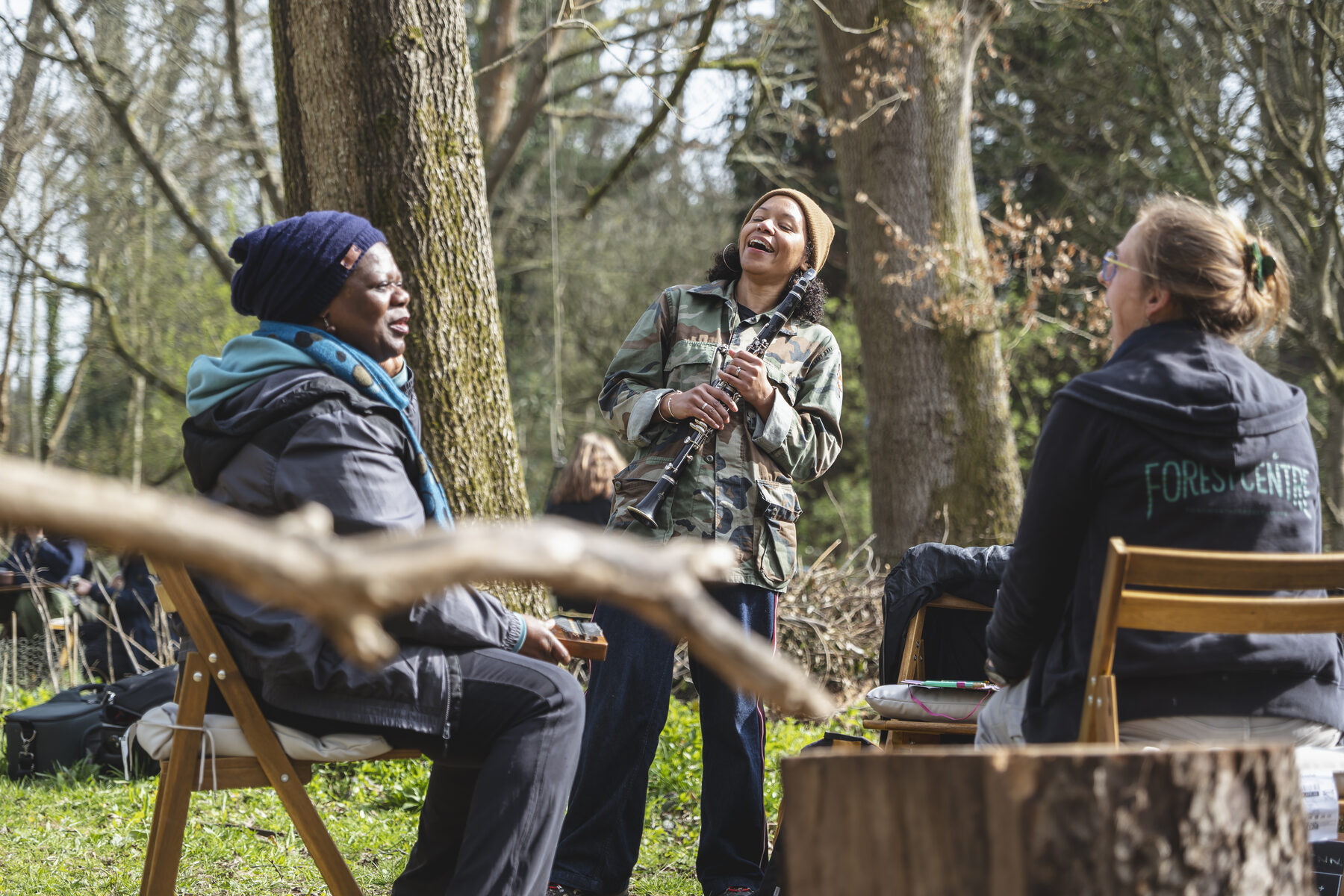 Three participants laughing together in woodland, one holding a clarinet